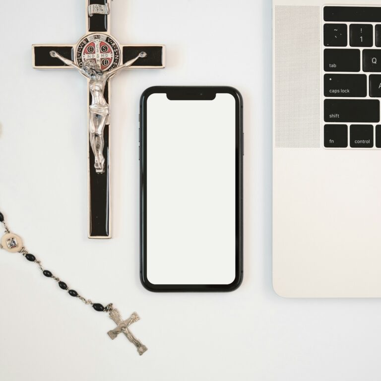 Crucifix, rosary, smartphone and laptop arranged on a table.