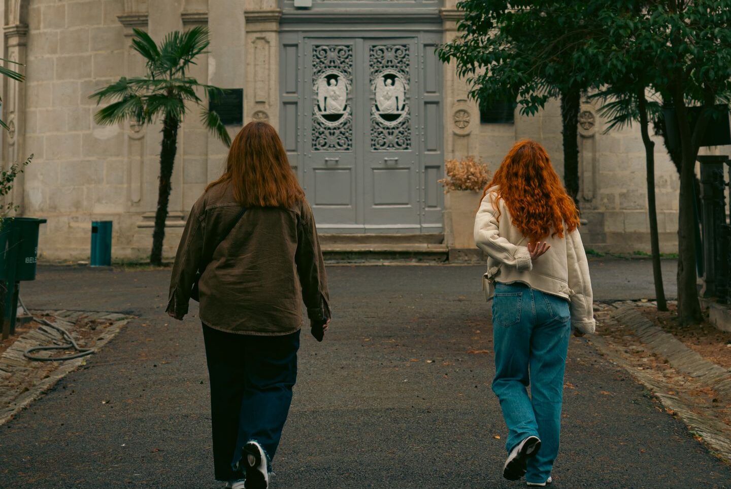 Two individuals approach a historic church with a red dome, surrounded by trees.